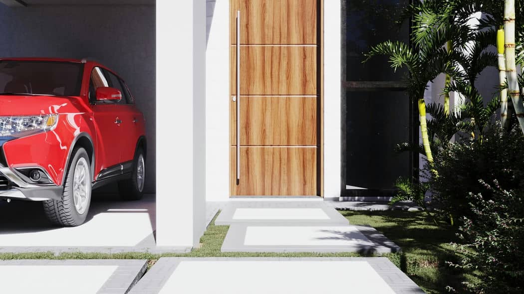 Um carro vermelho estacionado em uma entrada de casa moderna com folhagem verde ao redor.